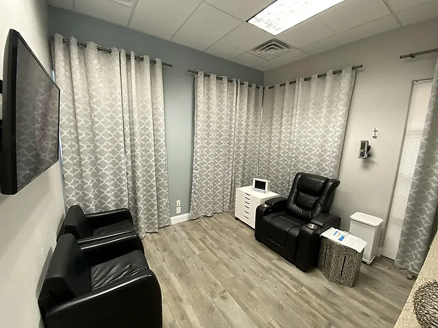 Clinic infusion room with black leather recliners, a side table and a wall TV