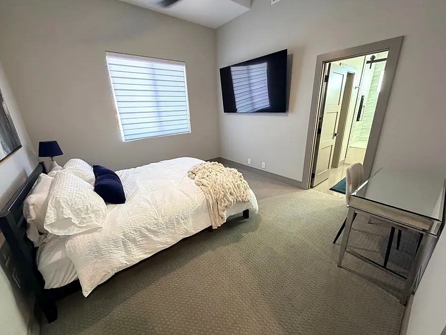 Bedroom at the house with plantation shutters, a white throw and a wall TV