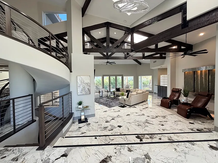 Great room seen from the staircase, with beams, a chandelier and lounge chairs