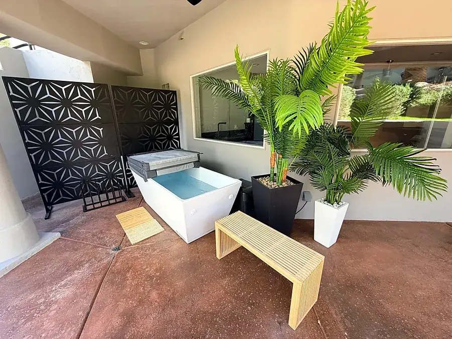 Wellness corner with a white soaking tub, palm plants and a wooden bench
