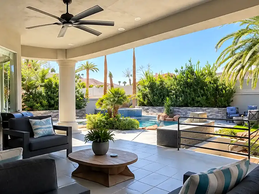 Covered patio with lounge sofas and a ceiling fan, looking out to palms and the pool